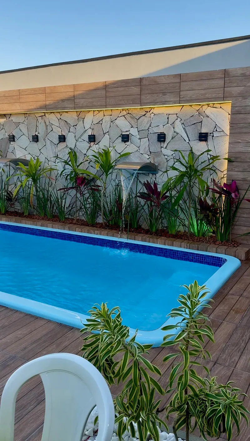 Piscina com cascata de água, parede de pedra com luz embutida e plantas ao redor