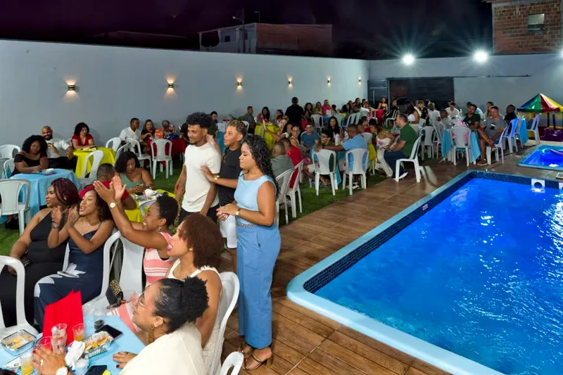 Festa à noite, com o gramado cheio de mesas e convidados ao lado da piscina