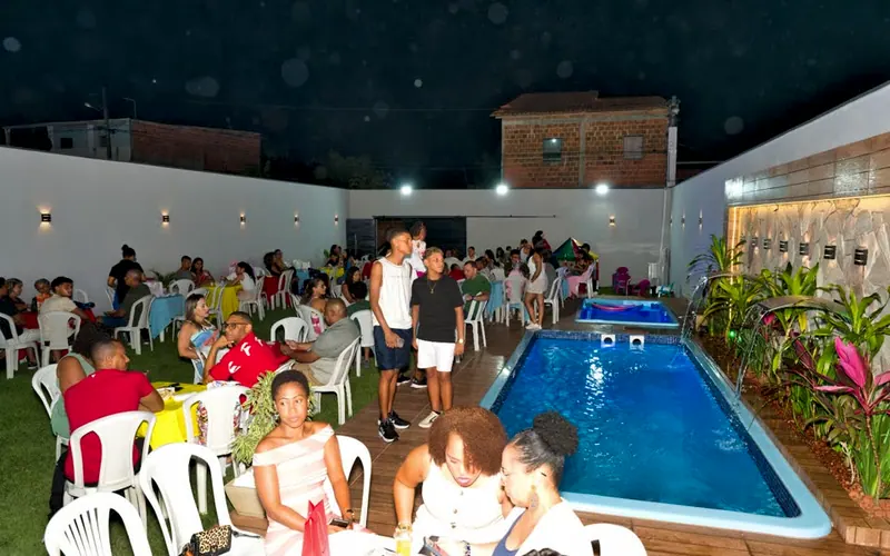 Festa à noite, com mesas e convidados pelo gramado e a piscina com a cascata à direita