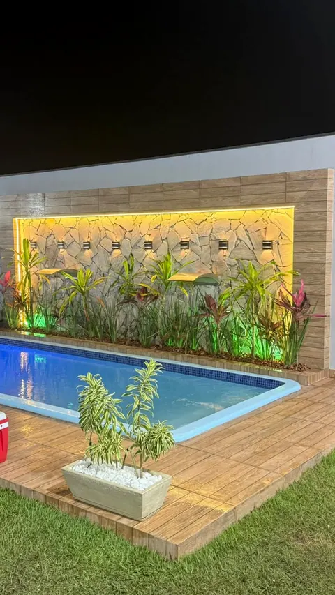 Piscina à noite, com a parede de pedra iluminada em amarelo e as plantas com luz verde